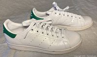 Side view of white Adidas Stan Smith sneakers showing green heel tab and slightly worn soles.