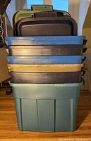 Stack of six Rubbermaid Roughneck plastic storage bins in mixed colors with lids on top.