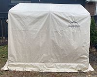 Front view of assembled beige Shelter Logic storage shed showing fabric cover and logo.