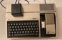 Top view of TI-99/4A computer with Speech Synthesizer accessory attached and power adapter on top.