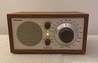 Front view of Tivoli Audio Model One radio showing speaker, tuning knob, volume knob, and indicators.