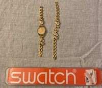 Full view of the Swatch watch with band and an additional band separated, shown with original branded case.
