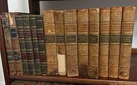 Front view of 12 leather-bound books, mostly Turner's History of England with some Modern History volumes and Creation and Deluge book in the middle. Varied spine conditions with visible wear and some missing parts.