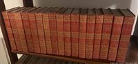 Photo of the full 18-volume book set showing red cloth bound spines with gold decorative floral pattern and titles.