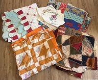 Antique quilts and linens arranged on wooden floor showing multiple patchwork quilts and smaller embroidered linens.