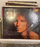 Front view of Barbra Streisand 'Wet' LP album on top of the stack, shows sticker price and image of Streisand with wet hair, wrapped in plastic sleeve.