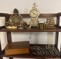 Shelf showing Art Deco light fixture, ornate clock, brass bookends, wooden box and flatware collection.