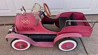 Side view of red metal pedal car showing pinstriped body, whitewall wheels, chrome headlamp and footboard