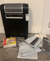 Photo showing Lasko ceramic heater with a box of soft white plastic magazine mailers and some folded white mailers next to it on carpet