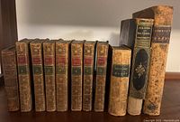 Front view of 11 antique leather bound books lined up on a shelf, including 7 volumes of Oeuvre de Moliere and separate titles with worn leather spines and gilt decoration.