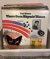 Front cover of Paul Simon's 'There Goes Rhymin' Simon' LP showing colorful abstract design with mask and stars.