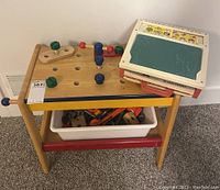 Photo showing wooden child's workbench with various wooden tools and a white plastic bin filled with hardware below. The Fisher Price School Days Desk toy is placed on top of the workbench.