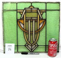 Front view of stained glass window panel with measuring items for scale, showing geometric Art Deco design in green, yellow, and brown glass with visible cracks.
