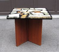 Front view showing square lucite top with stone fragments and wooden base in an X-shape.