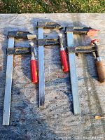 Three clutch style woodworking clamps laying on a wooden surface, showing their size and condition.