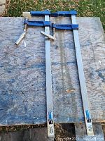 Two 24 inch Mastercraft F-clamps lying on a wooden surface outdoors
