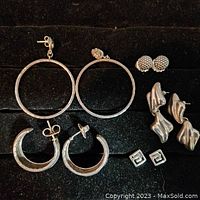 Full view of six pairs of earrings displayed on black velvet. Includes variety of hoop and stud styles all in silver tone.