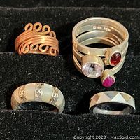 Five ladies rings arranged on black fabric, showing variety of metals and gem set design