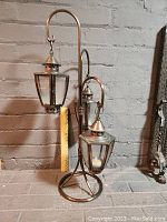 Full view of a metal decorative candle lantern stand holding two lanterns with clear glass panes and peaked tops.