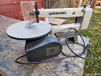 Side view of Dremel scroll saw showing metal work table, blade area, motor, and power cord.
