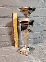 Full side view of the tall silver tone candle holder next to a measuring stick showing height