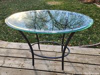 Front angle view of oval glass top table showing intact glass and metal frame on wooden deck outdoors.