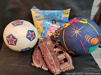 Soccer ball, basketball, baseball glove, and inflatable float in original package arranged on a black surface.