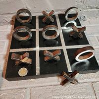 Front view of black wooden tic-tac-toe board with silver metal X's and O's in play, grid clearly visible, coin for scale.