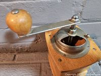 Close-up of the metal crank handle with a rounded wooden knob on a wooden coffee grinder.