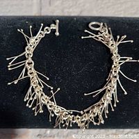 Front view of vintage silver charm bracelet with delicate dangling wire charms tipped with small beads, displayed on black background.