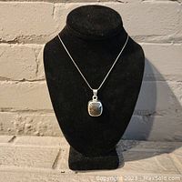 Full view of the vintage necklace displayed on a black stand against a brick background.