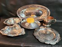 Overview of six silverplate pieces including tray, cup, bowl, candle holder, and two dishes