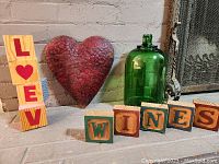 Front view of red heart-shaped metal decor, green glass bottle, and wooden blocks spelling LOVE and WINES.