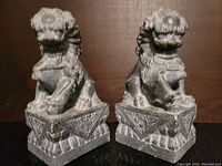 Front view of both stone mythical lion carvings side by side showing their detailed faces and bases.