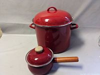 Large red enamel stock pot with matching lid and two side handles, placed behind the smaller pot.