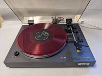 Side view showing the black turntable with red vinyl record and the tonearm with stylus.