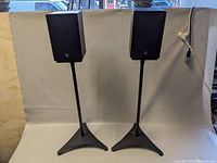 Pair of Boston CS23 speakers on black metal stands with tripod base in front of white backdrop