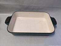 Rectangular enamel lasagna tray, interior off-white with green outer sides and black handles marked with 'Michael Smith.' Shows surface wear and scratches.