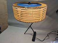 Full view of lamp showing round patterned fabric shade, blue metal diffuser inside, and black tripod base with weighted foot.