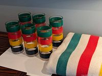 Photo showing 6 tall cylindrical glasses featuring clear glass with colored horizontal stripes: green, red, yellow, and black.