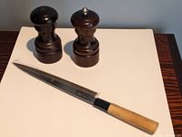 Full view of salt and pepper grinders with Japanese chef knife on flat surface