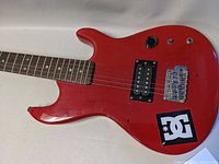Close-up view of guitar body showing red finish, humbucker pickup, volume knob, switch, and DC sticker