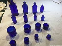 Overview of all 16 cobalt blue bottles and jars arranged on white surface.