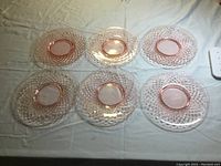 Set of six pink Depression glass luncheon plates arranged side by side on a white surface.