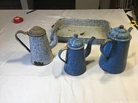 Full view of three antique enamel coffee pots and blue enamel roast pan on table.