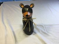 Front view of the black bear wooden carving with raffia bow on neck.