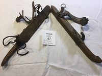 Pair of antique strap-on ice skates showing wooden platforms and steel blades laid on white cloth with a label reading '47 Vintage Ice Skates'.