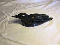 Side profile of the black stone loon carving on a light fabric background showing elongated beak and body with etched feather details.