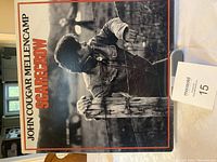 Front cover of John Cougar Mellencamp's 'Scarecrow' LP showing a black and white image of the artist by a fence.