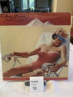 Front cover of The Rolling Stones LP Made in the Shade showing woman in swimsuit with headphones and eye mask lounging on chair